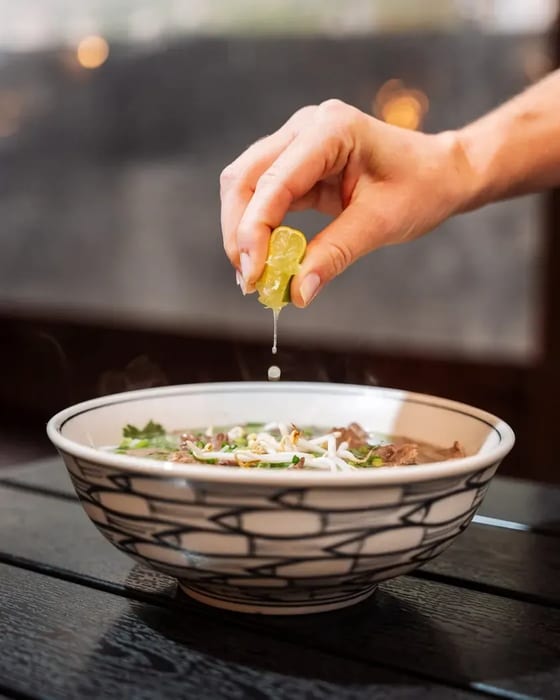 Ruka vymačkává limetku do misky phở