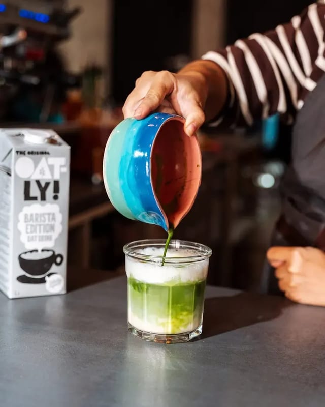 Barista nalévá matchu z modré misky do sklenice s mlékem